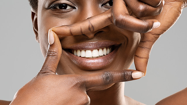 The image shows a person smiling with their hands positioned over their eyes, creating a heart shape with their fingers.